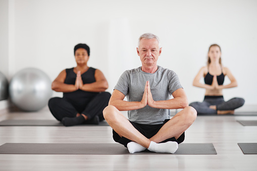 Portrait of senior man sitting in lotus position and meditating during yoga class in studio