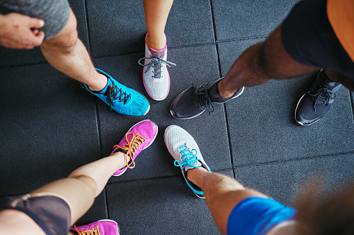 High angle of a group of sporty people's feet wearing running shoes standing together in a huddle on a gym floor
